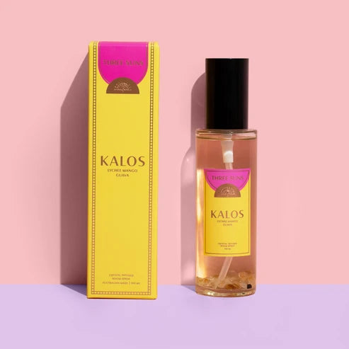 A bottle of Kalos room spray with a black cap stands next to its yellow packaging box on a pink and lavender background. The box and bottle label feature a bright pink top section and the brand name &