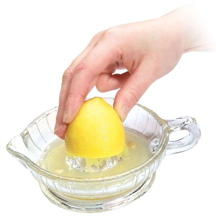 Hand using a glass lemon squeezer to extract juice from a lemon on a white background
