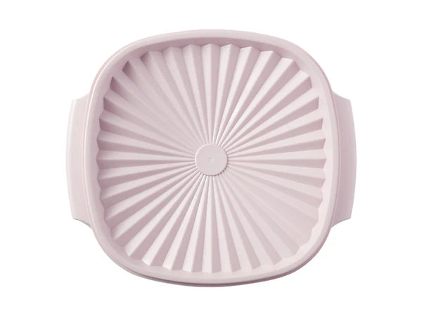 A light pink silicone baking pan with a sunburst fluted interior and side handles, shown from a top-down view on a white background.