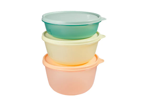 Three stacked round plastic bowls with matching lids in pastel shades of peach, pale yellow, and mint green, isolated on a white background.