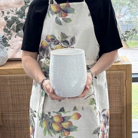Person holding a white textured utensil pot wearing a floral apron.
