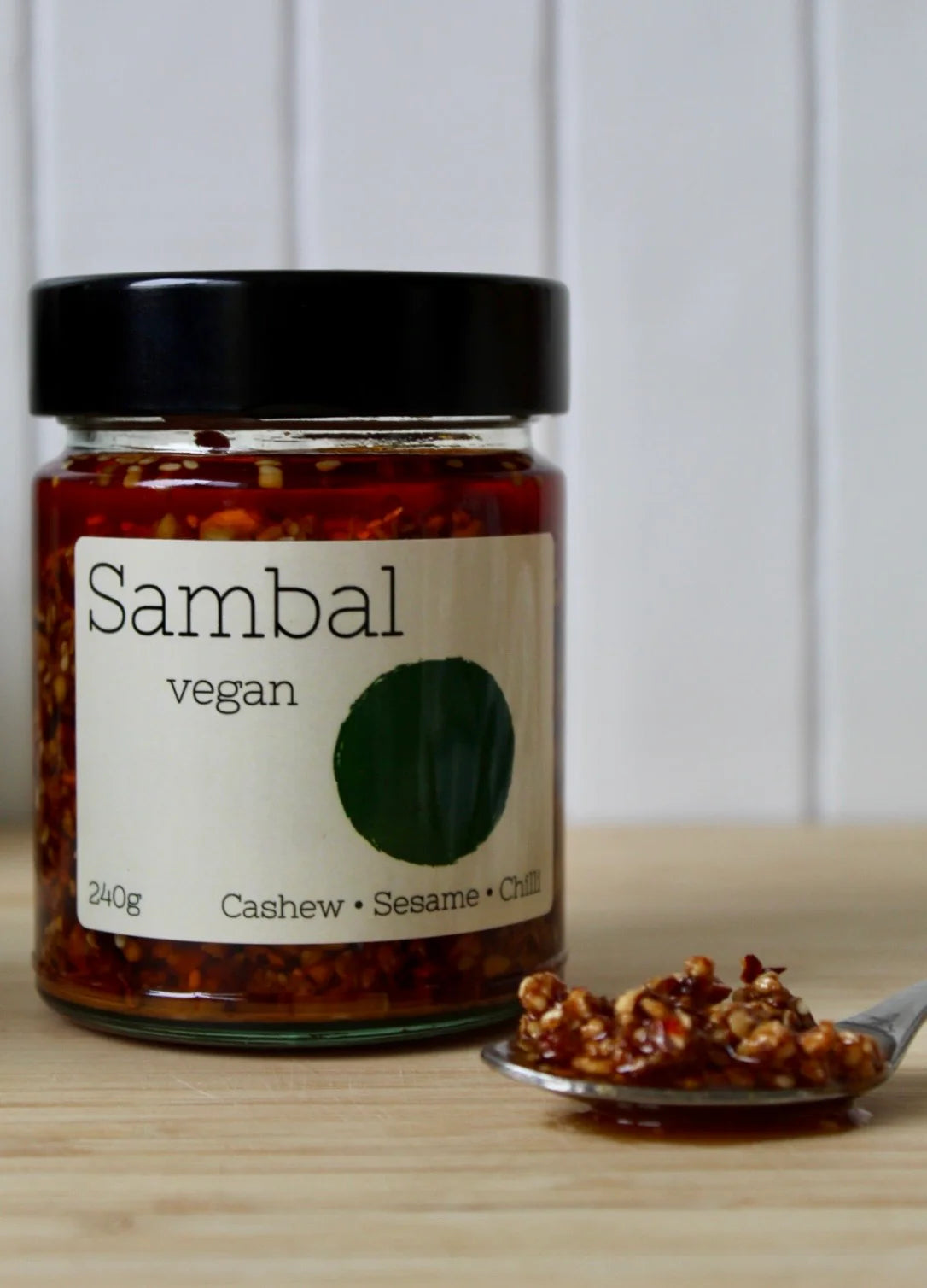 Jar of vegan sambal with a spoonful of sambal on a wooden surface.