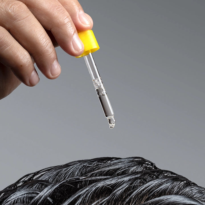 Hand holding a dropper with a clear liquid above hair, on a gray background