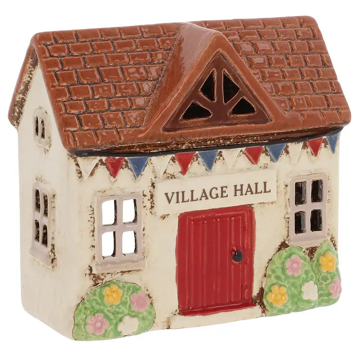 A ceramic house tealight holder with the words Village Hall with plants and bunting