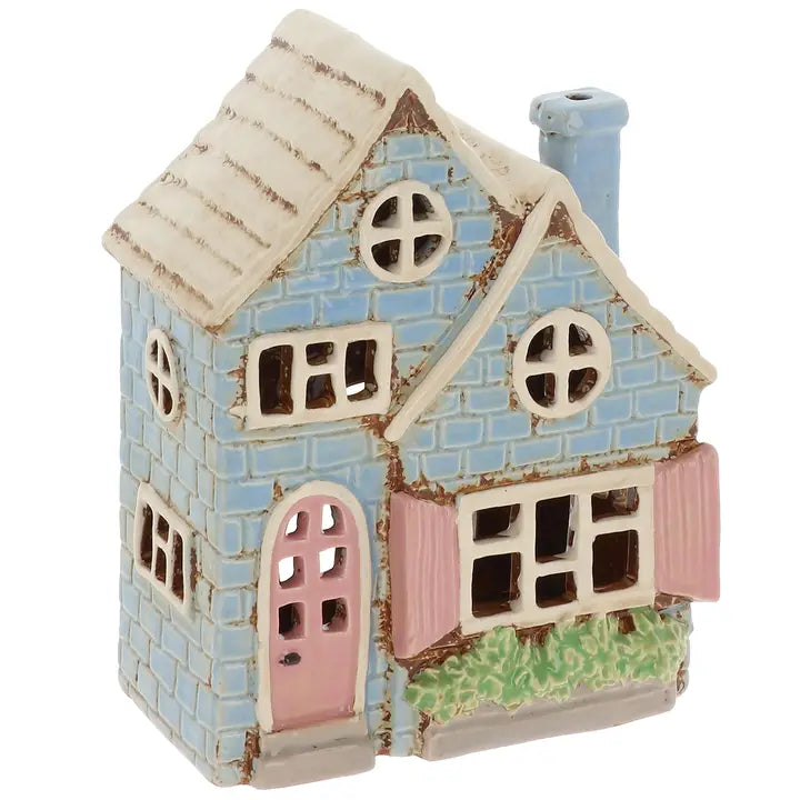 Decorative tealight house with blue brick facade, pink door, and white roof on a white background