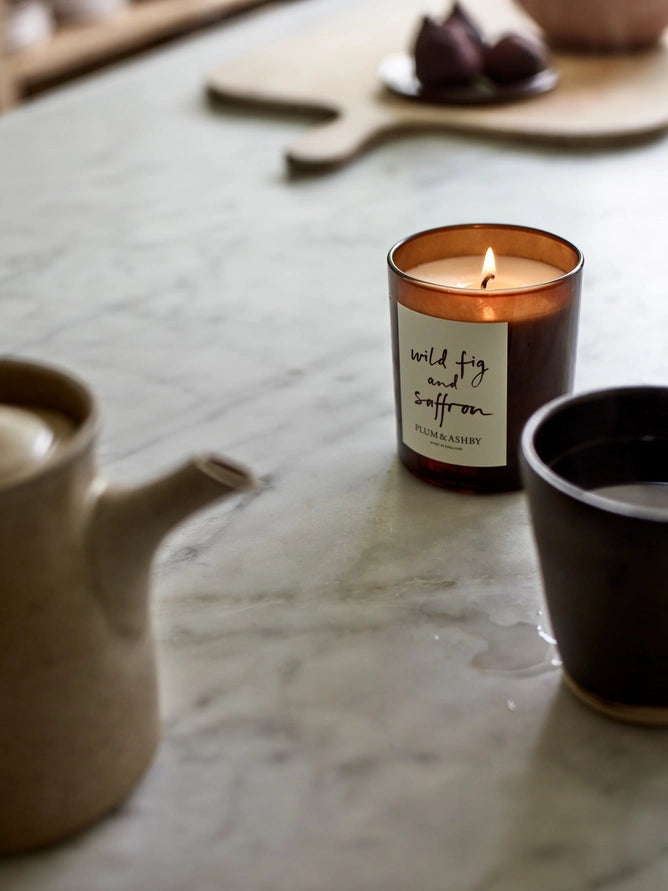 Lit candle with label wild fig and saffron by Plum and Ashby, on a marble benchtop