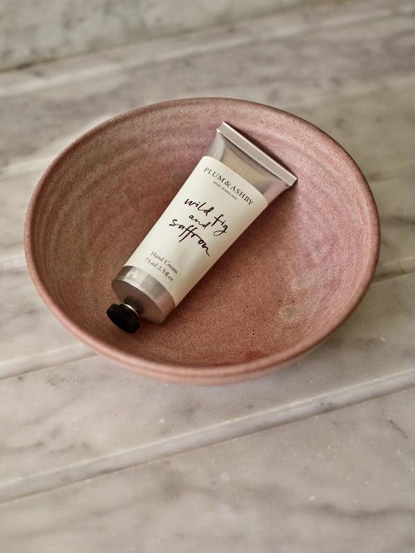 Tube of wild fig and saffron hand cream in a pink clay bowl on a marble table