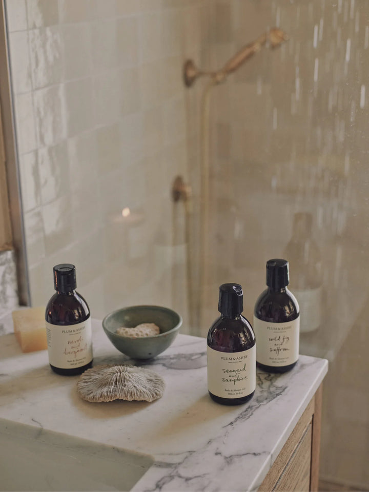 Amber bottles of body wash shower gel on a marble bench in a bathroom with neutral tiles
