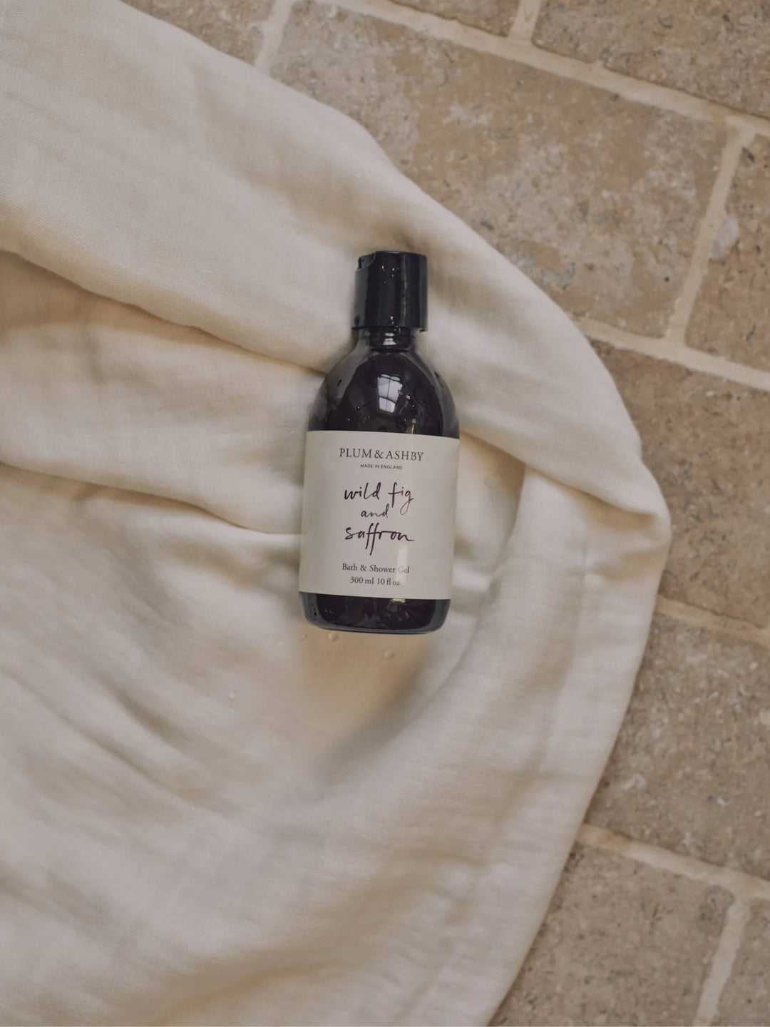 Wild fig and saffron bath and shower gel on a cream coloured linen on a brick background