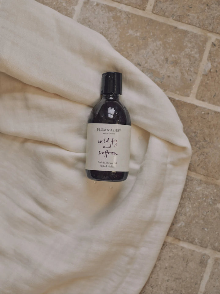 Wild fig and saffron bath and shower gel on a cream coloured linen on a brick background