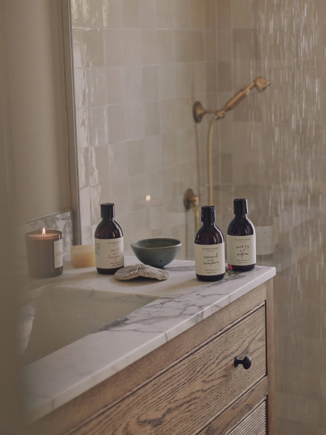 Group of amber bottles of bath and shower gel in a neutral coloured bathroom with shower in the background