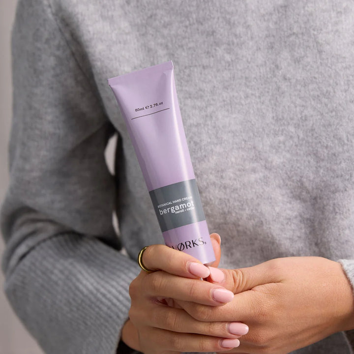 Person holding a purple tube of skincare product with &