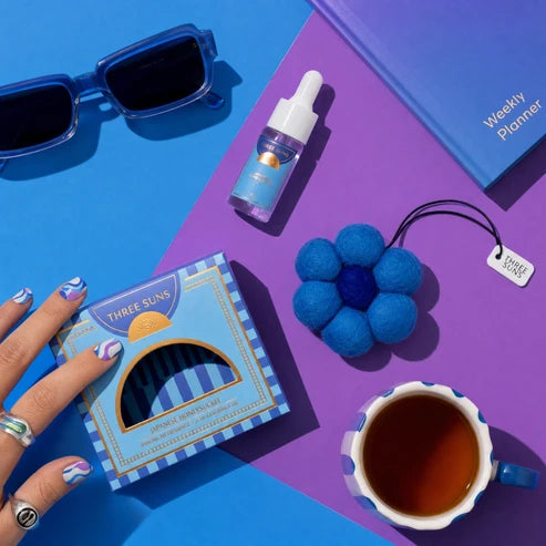 Blue sunglasses, bottle, flower-shaped object, and cup on a blue and purple background