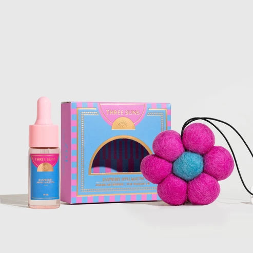 Three Suns Zoi Air Freshener featuring a pink dropper bottle, a colorful blue and pink gift box, and a pink felt flower diffuser with a blue center on a white background.